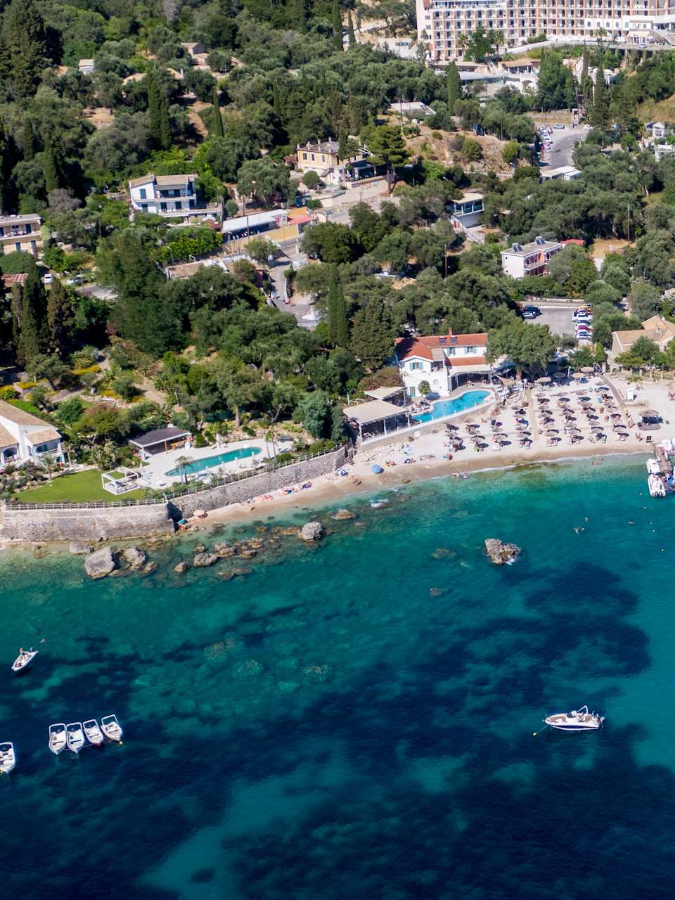 Blick auf einen Strand an türkisem Wasser mit Bäumen und Häusern im Hintergrund